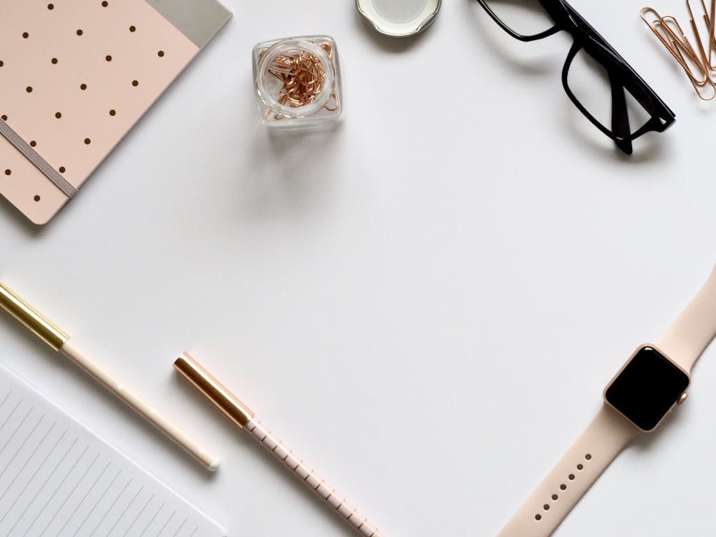 Stylish rose gold themed flatlay featuring office supplies and a smartwatch on a white background.